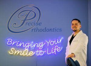 Orthodontist standing on the side the Precise Orthodontics neon sign.