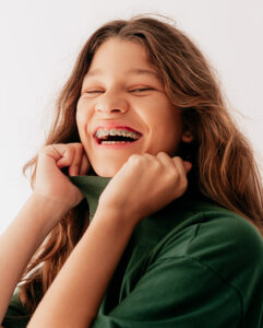 Little girl smiling with braces and holding her shirt