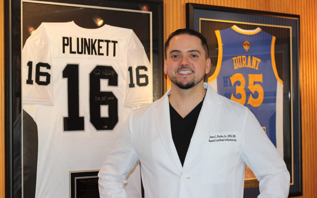 Spanish speaking Dr standing next to two jerseys in office.