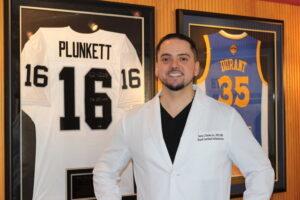 Spanish speaking Dr standing next to two jerseys in office.